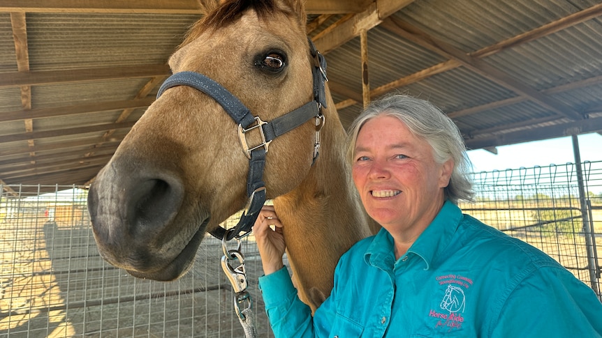 A woman stands in a stable, holding a horse.