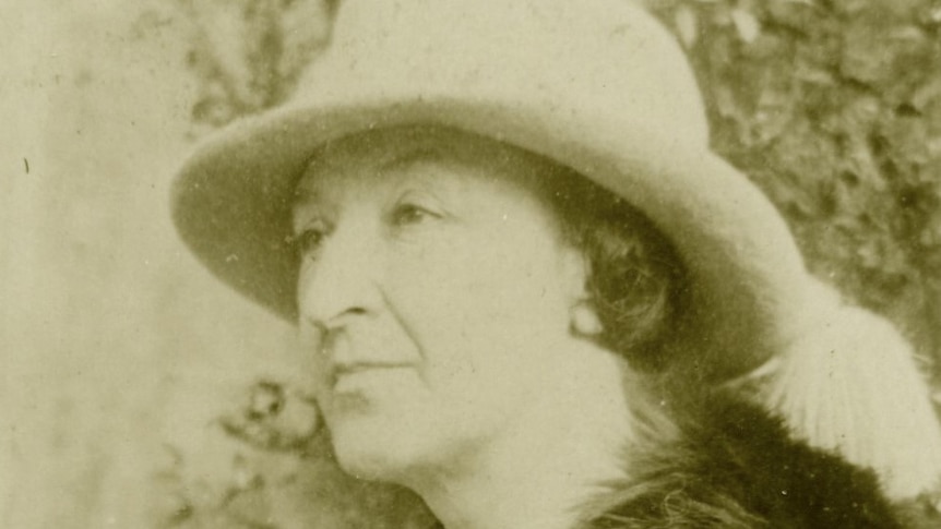 Woman with fur coat and a hat stares into the distance while sitting down.