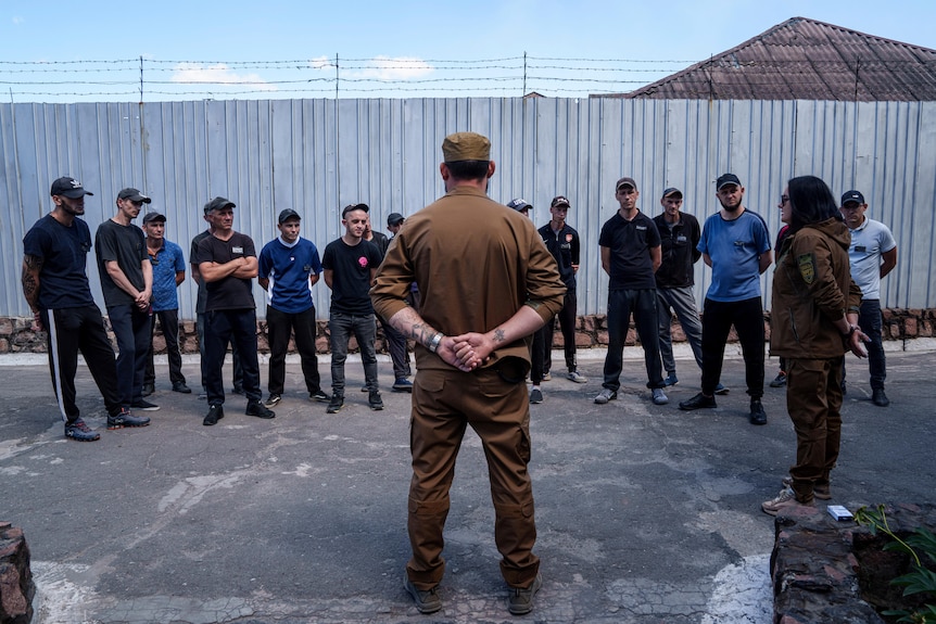 Men stand in a semi-circle and listen to an Ukrainian sergeant