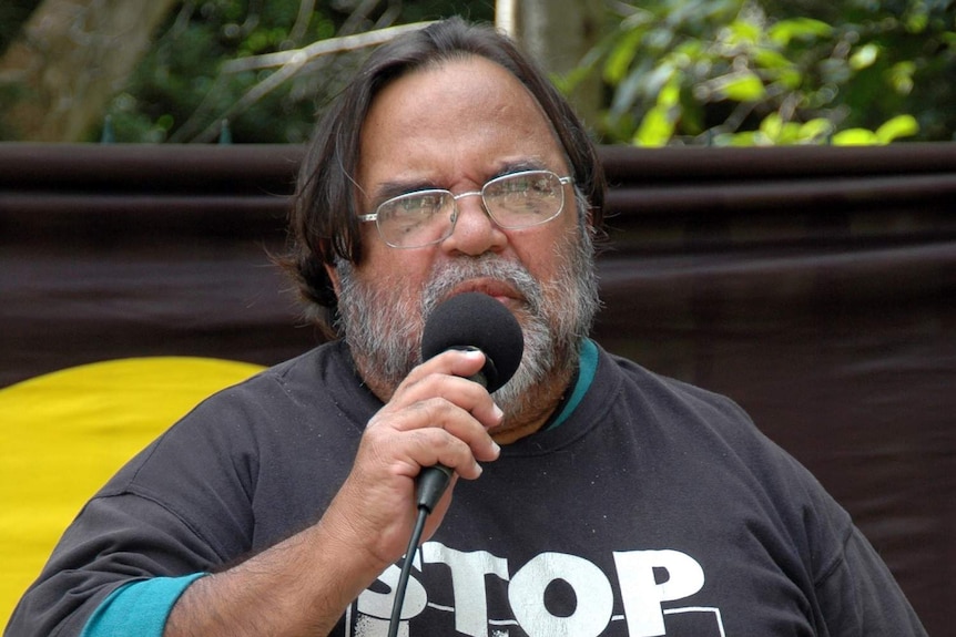 Aboriginal activist Sam Watson addresses a small crowd with Aboriginal flag in background.