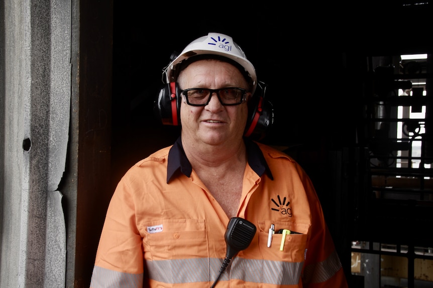 A man in high vis and a white hard hat looks to the camera