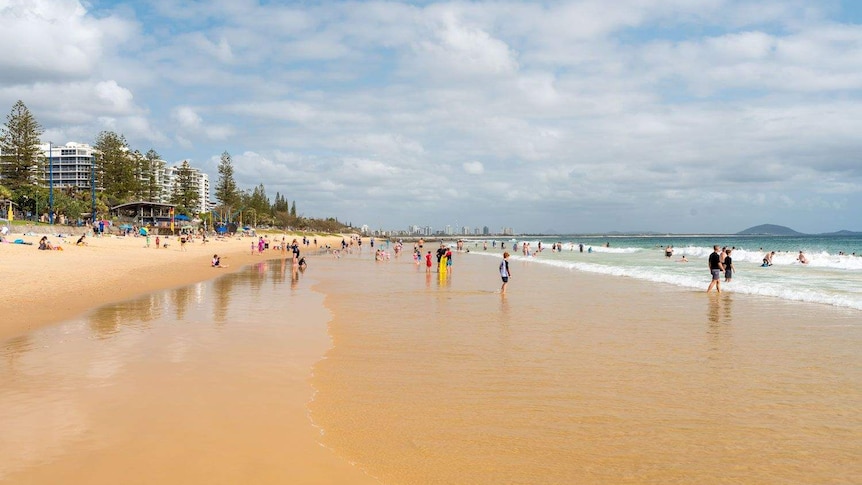 A wide shot of Mooloolaba Beach with people dotted across the sand and in the water.