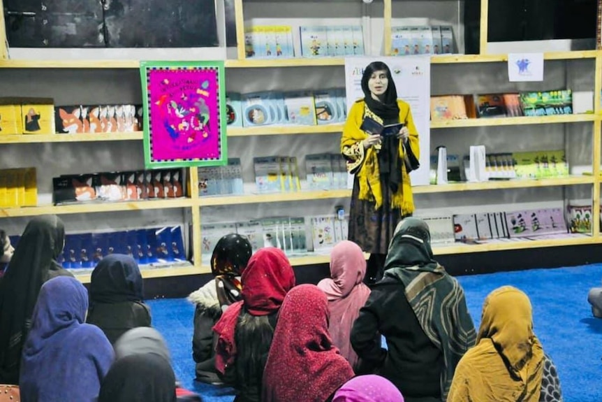 Una foto de una mujer joven parada en el salón de clases frente a un grupo de estudiantes 