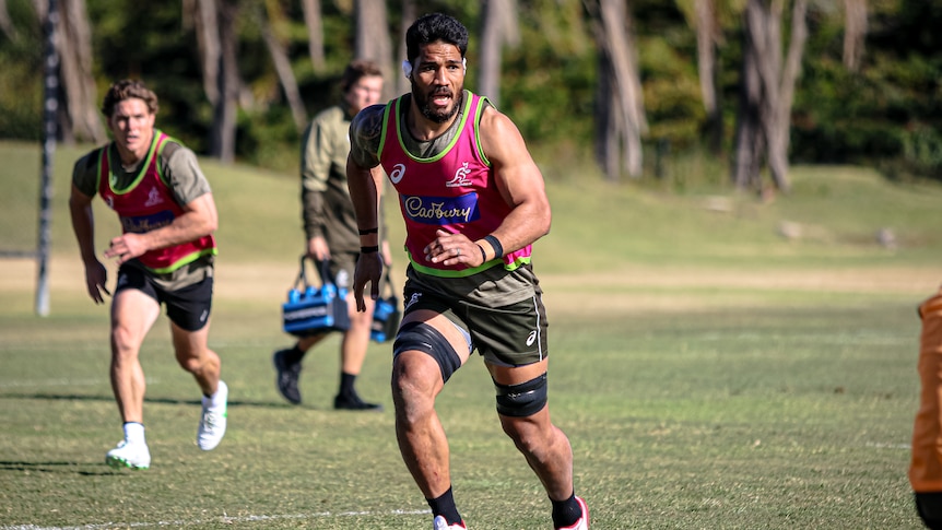 Sitaleki Timani runs at Wallabies training with Michael Hooper in the background.