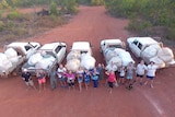 A group of Nhulunbuy residents standing in front of utes packed with rubbish, looking up at a drone.