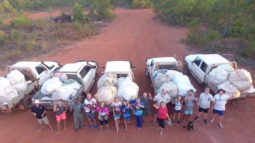 A group of Nhulunbuy residents standing in front of utes packed with rubbish, looking up at a drone.