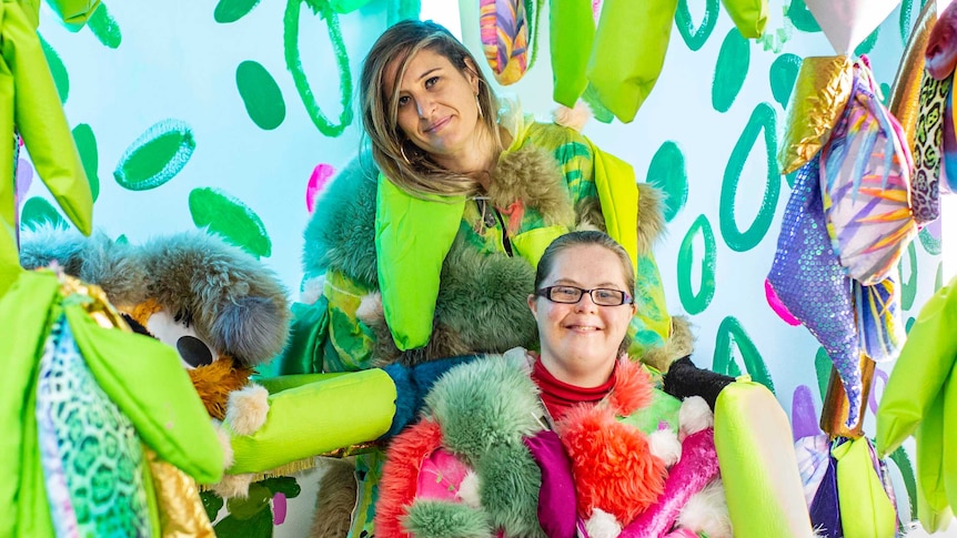 The two artists, wearing multi-coloured furry costumes, stand in their psychedelically coloured installation.