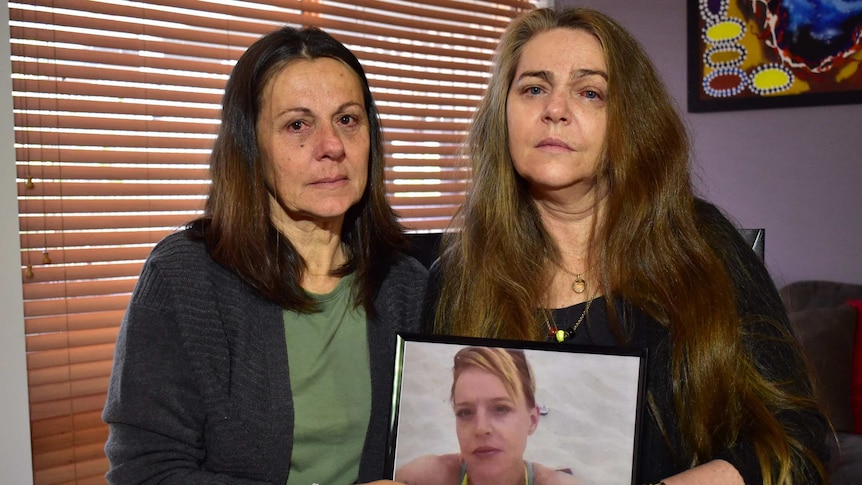 Kym's mother and aunt hold a framed photograph of her.