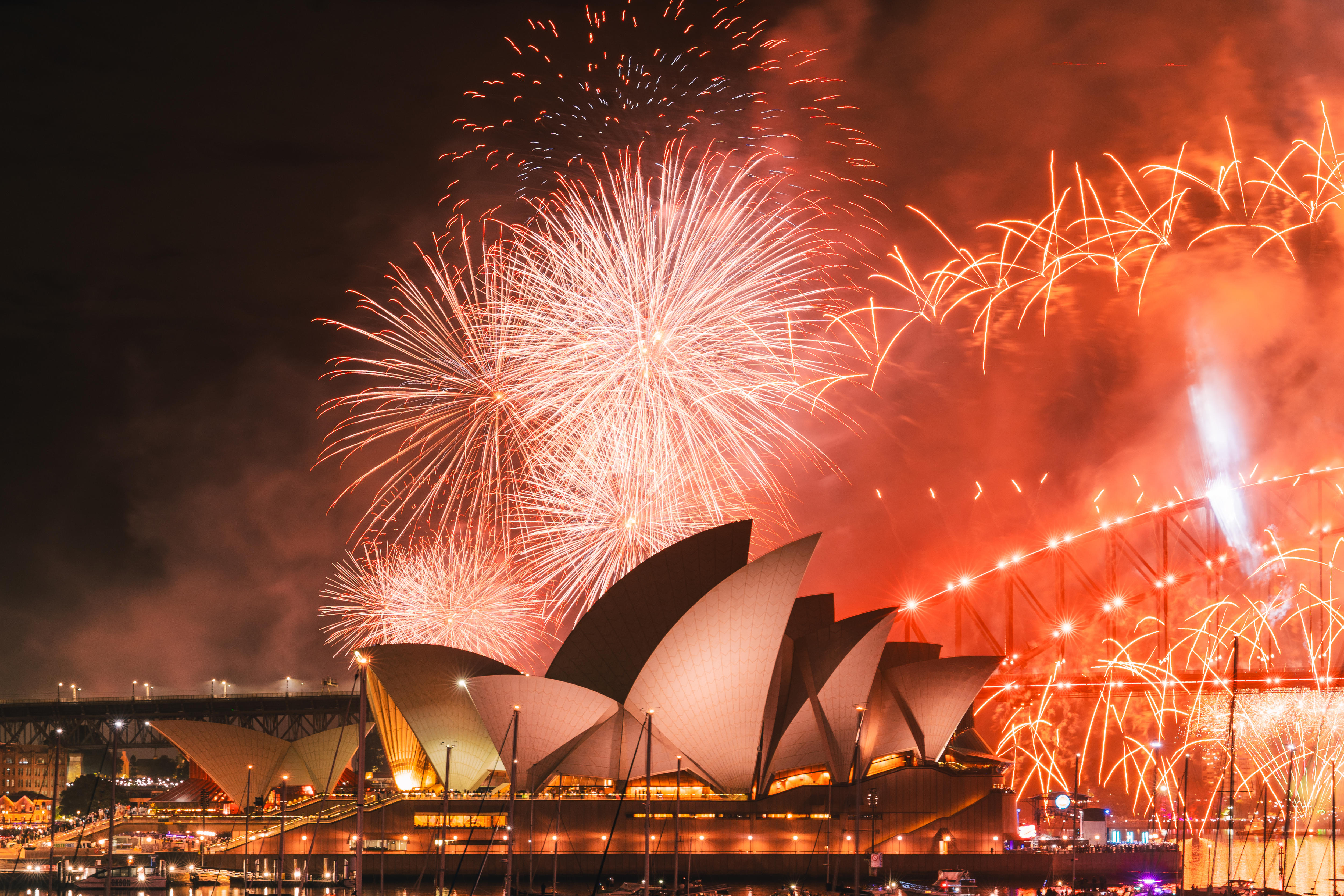 Las grandes estructuras blancas en forma de velas de la Ópera de Sydney están iluminadas por fuegos artificiales rojos.