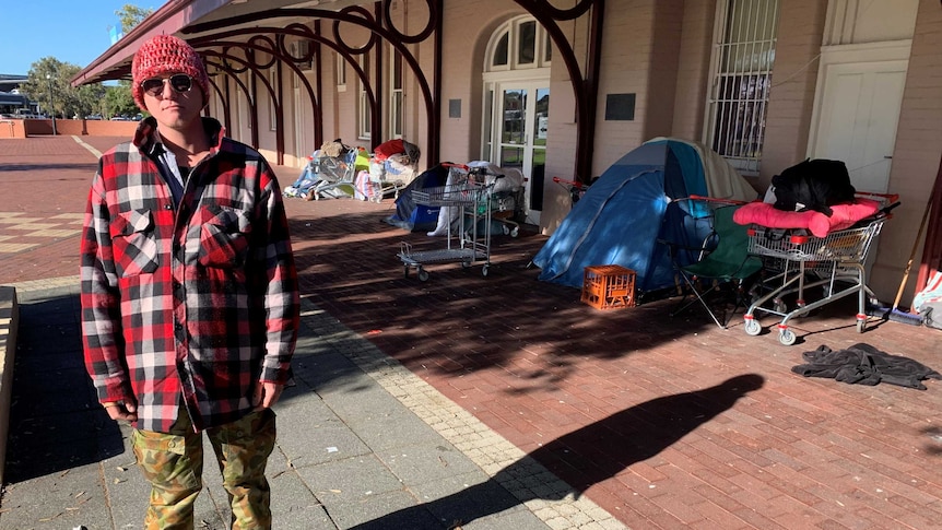 Jack is homeless and is standing in front of the tent where he sleeps.