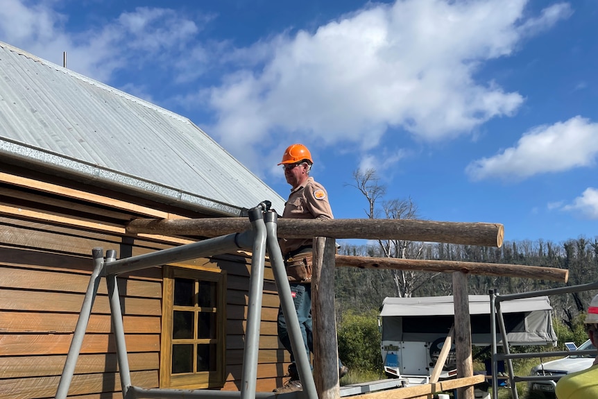 A man in hardhat stands on scaffolding adjacent a tin roof