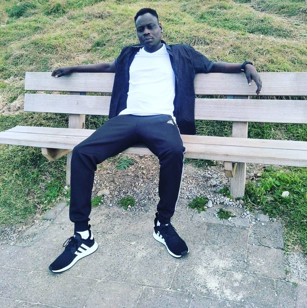 African Australian young man seated on a park bench in casual clothing