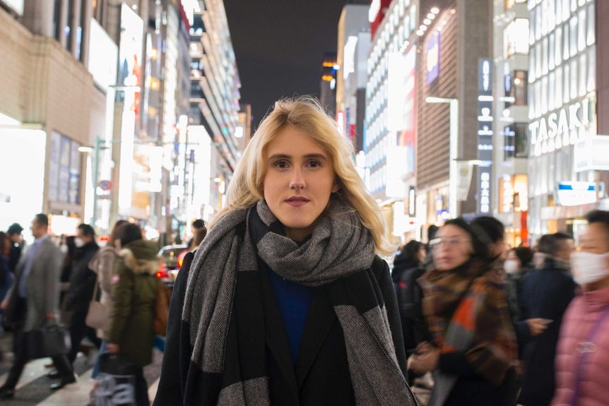 Justine Landis-Hanley standing on the street in Tokyo at night with people, lights and building in the background