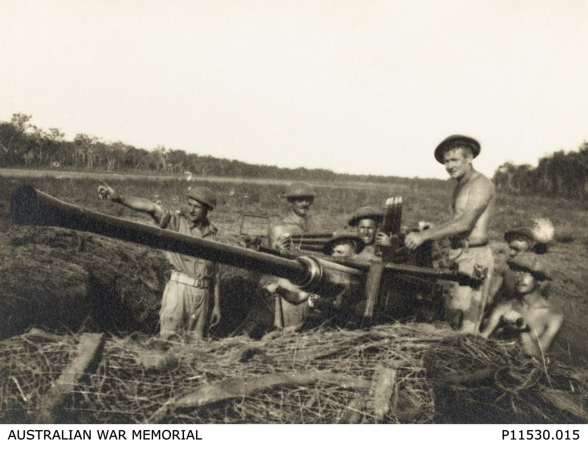 A historical black and white photo showing a group of men around a WWII-era cannon gun, in a field. 