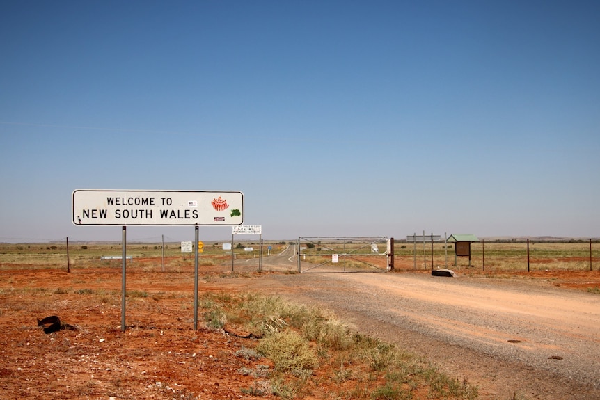 A big sign reads Welcome to New South Wales in front of a fence on a road. 