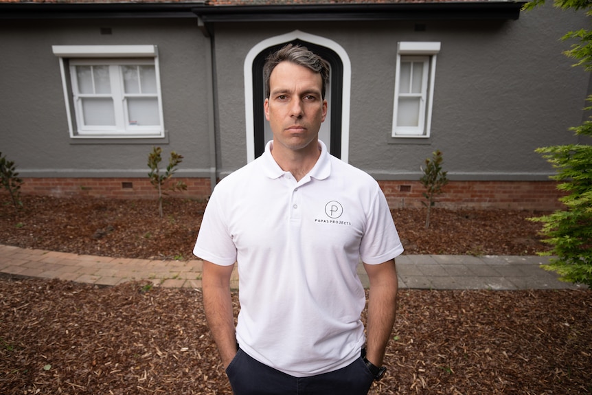 A man stands outside a house. He looks serious.