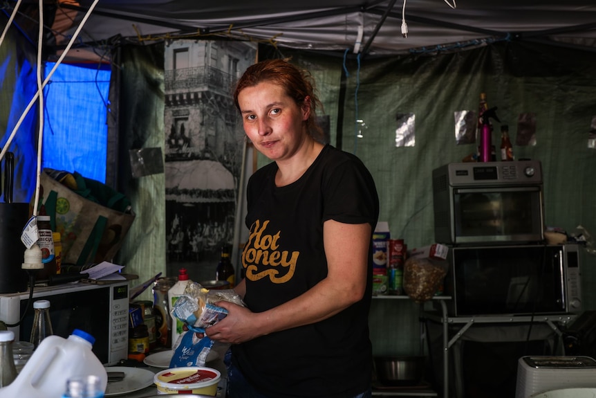 A woman in a tent holding bread with a tub of margarine nearby.