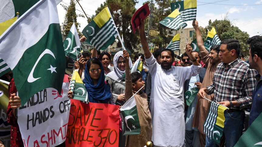 A group of Pakistani people gather, waving flags and holder posters as part of an anti-Indian protest
