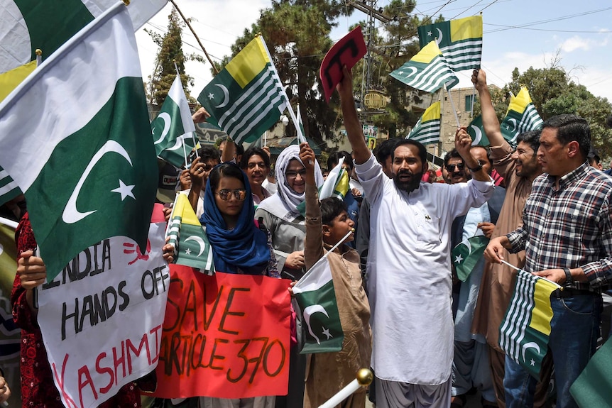 A group of Pakistani people gather, waving flags and holder posters as part of an anti-Indian protest