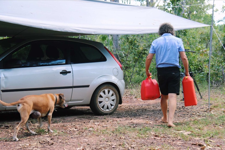 Andrew Walton carries to red jerry cans to his car as his dog follows him