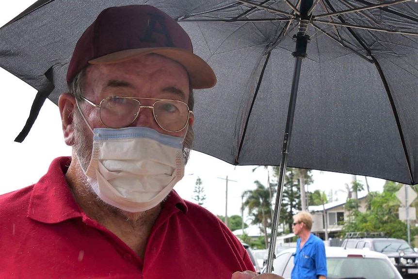 A man in a face mask holding an umbrella