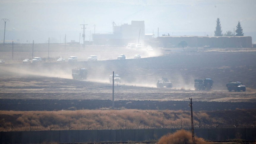 More than a dozen Russian and Turkish military vehicles drive in procession on a dusty road