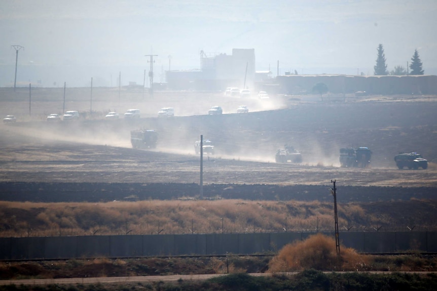 More than a dozen Russian and Turkish military vehicles drive in procession on a dusty road