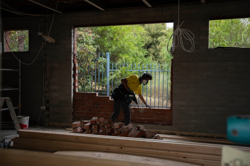 A man wearing construction gear builds a brick wall