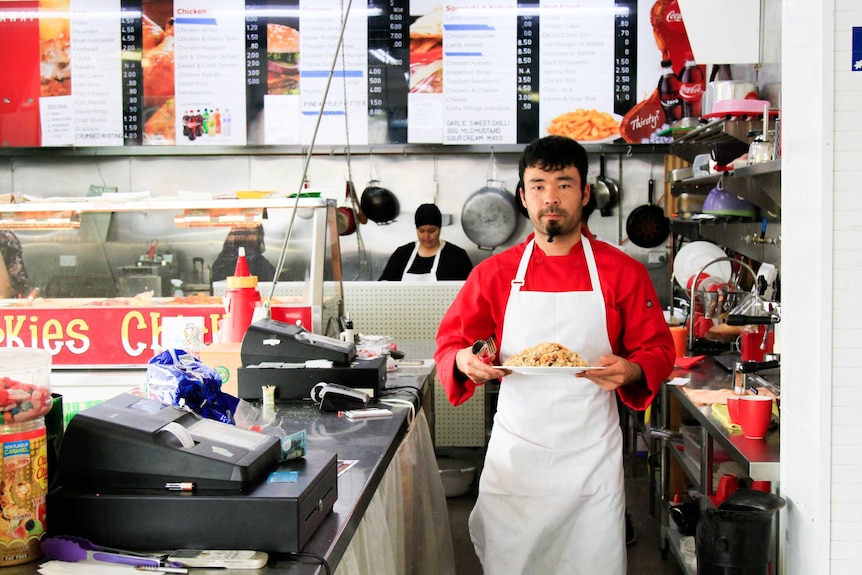 Amin Safa carries a plate of food through a takeaway shop