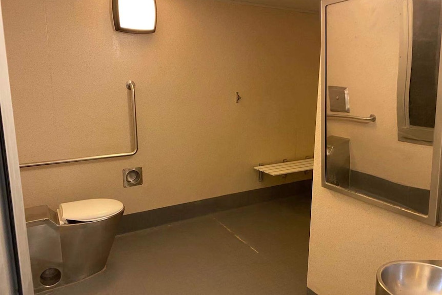 A sparse bathroom at the Christmas Island detention centre, the toilet is metal with a plastic lid, and it has no natural light.