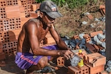 A tanned tradie squats for a tea break from his strenuous work.