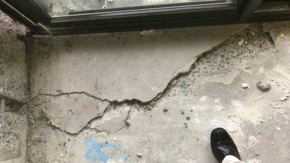 A concrete floor next to a glass sliding door appears significantly cracked. A person's show is visible in the corner of shot.