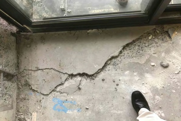 A concrete floor next to a glass sliding door appears significantly cracked.