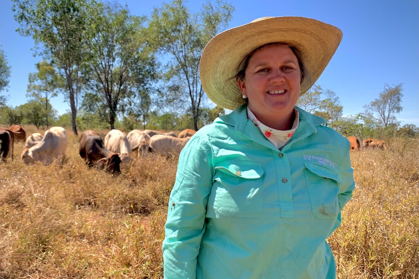 Photo of Grazier Kylie Stretton smiling. Her cattle are in the foreground. 
