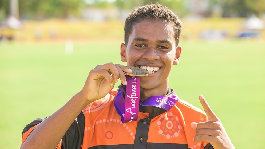 A young man biting his gold medal and smiling.