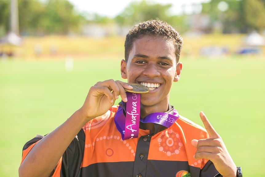 A young man biting his gold medal and smiling.