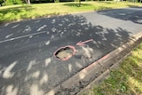 A deep pothole with pink drawing around it and an arrow pointing at it.