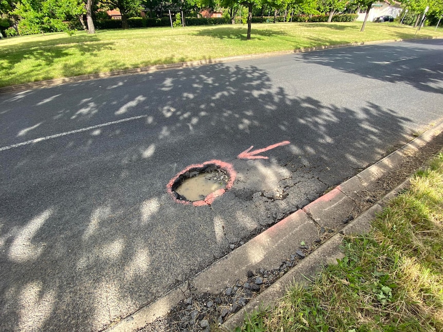 A deep pothole with pink drawing around it and an arrow pointing at it.