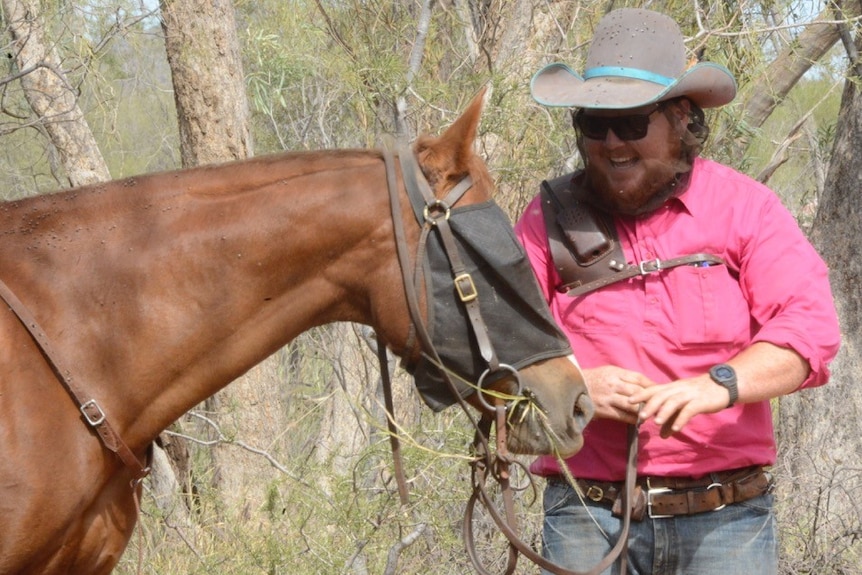 a man standing at the front of a horse wearing a fly net over its face