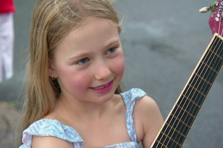 8 year old girl holds a guitar in the rain
