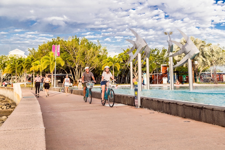 Pathway next to lagoon pool with elderly couple riding on bikes and young women walking in the background