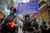 police officers wearing face masks on a Hong Kong street with one holding up a blue banner with a police warning written on it