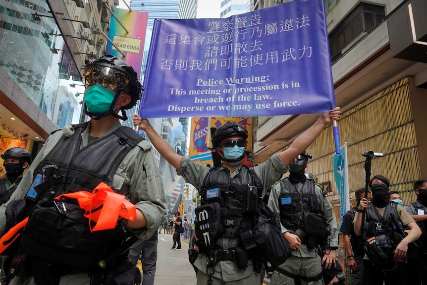 police officers wearing face masks on a Hong Kong street with one holding up a blue banner with a police warning written on it
