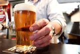 A man's hand serves a pint at a bar.