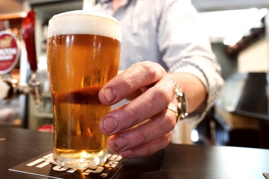 A man's hand serves a pint of beer onto one of Brooke Littlewood's coasters at the bar.