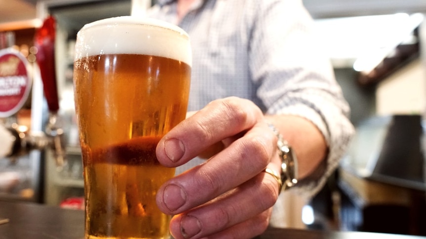 A man's hand serves a pint of beer onto one of Brooke Littlewood's coasters at the bar.