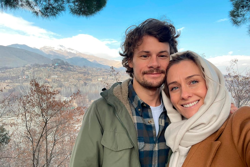 A woman and a man take a selfie in front of mountains