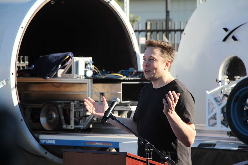 Elon Musk speaks at the Hyperloop pod competition in front of a hyperloop tube and pod prototype.