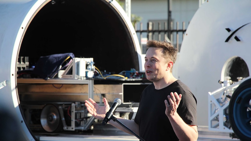 Elon Musk speaks at the Hyperloop pod competition in front of a hyperloop tube and pod prototype.