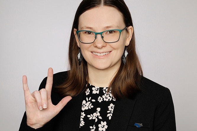 A smiling woman makes the Auslan sign for Deaf pride.